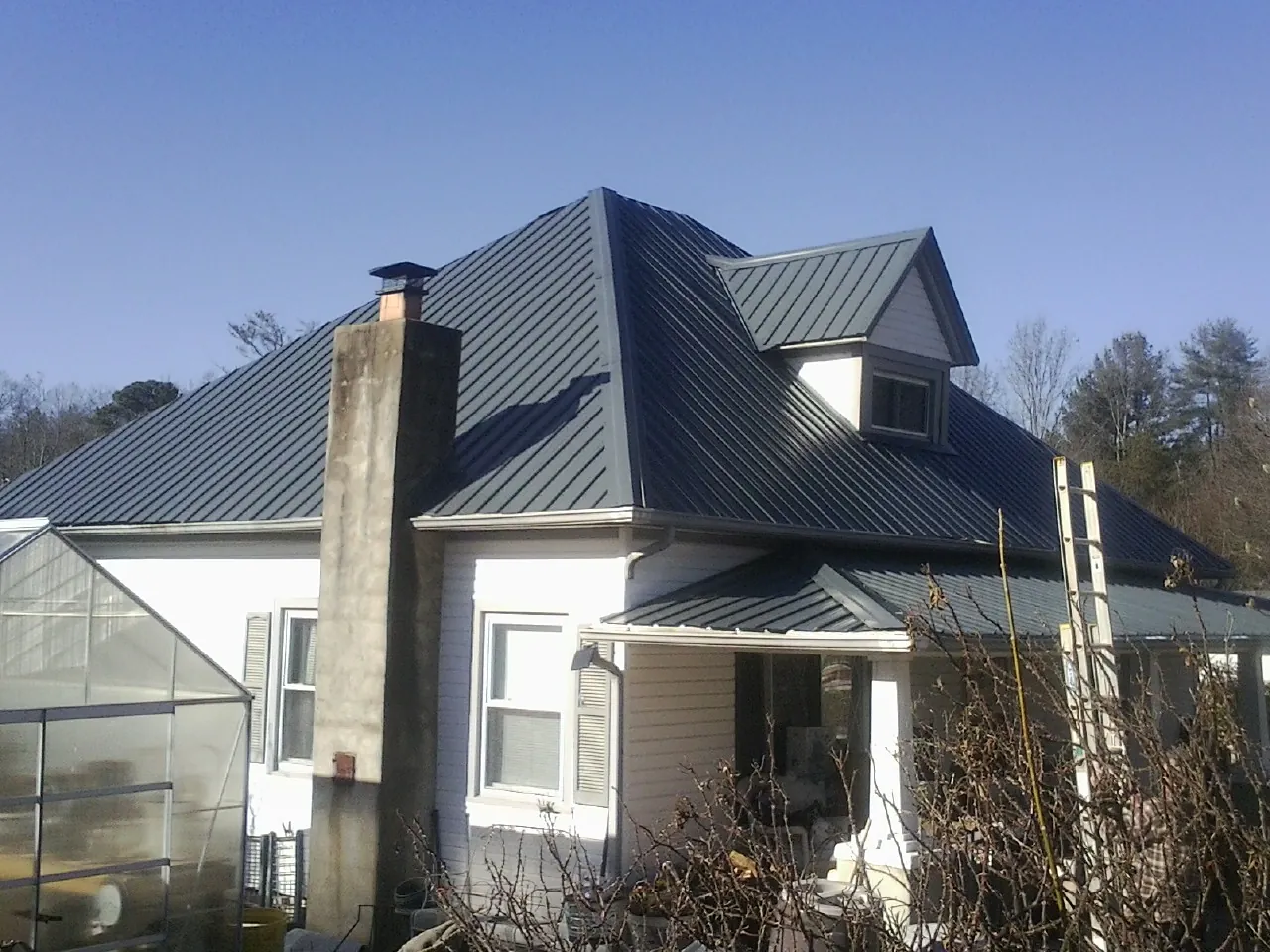 Dark blue standing seam metal roof on a white farmhouse with dormer — Slate & Tile Roof Repair by Roofing Brothers in Grantsville