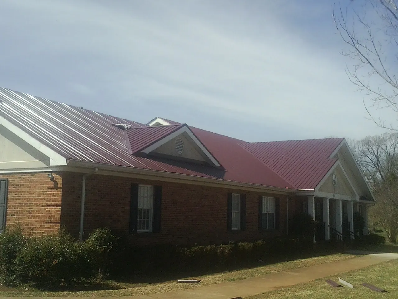 Red metal roof with gabled entries on a long brick building, from a Hail Damage Roof Repair job in Grantsville