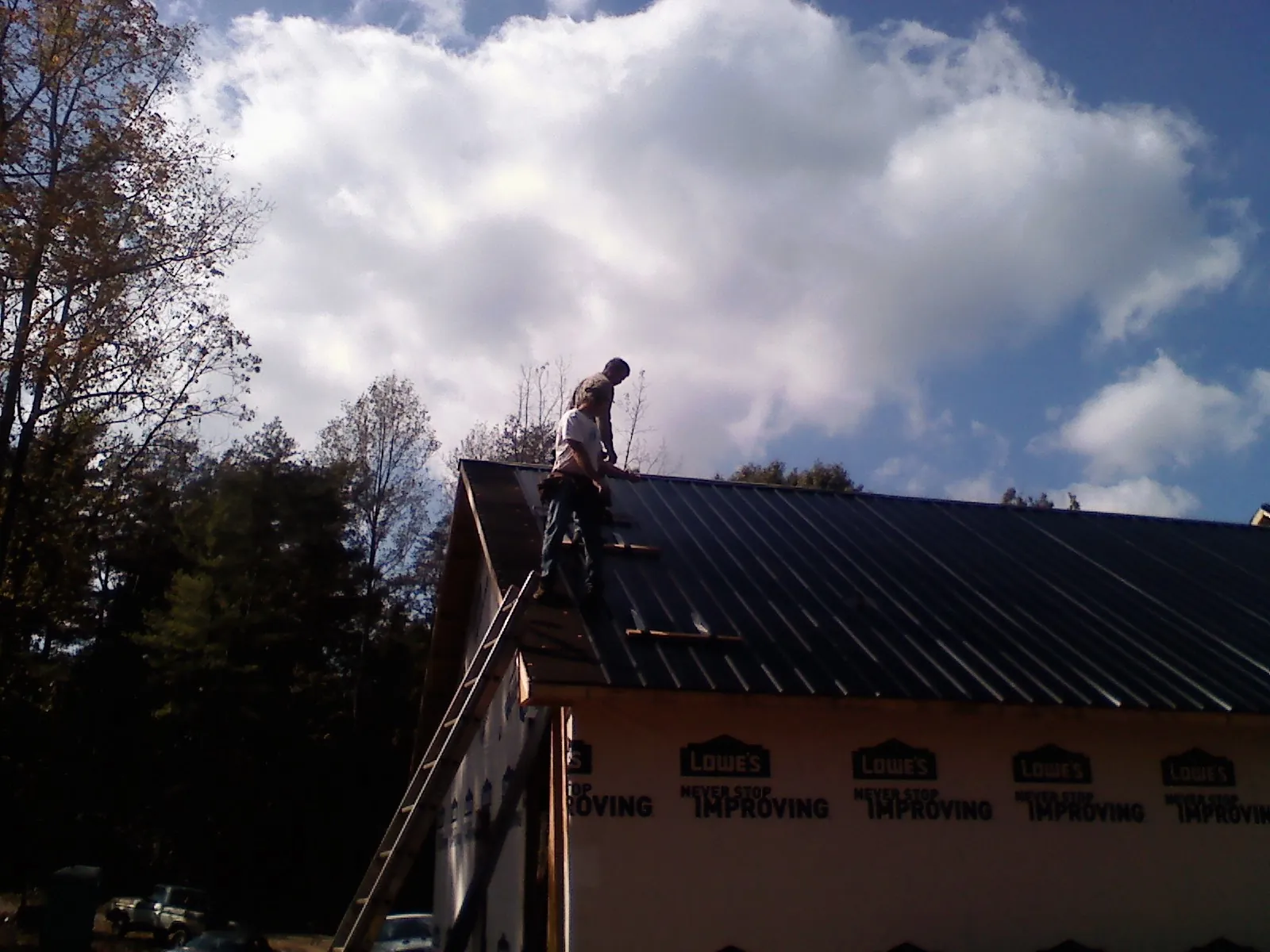 Roofer fastening dark metal panels high against a cloudy sky, from a Roof Inspection job in Grantsville